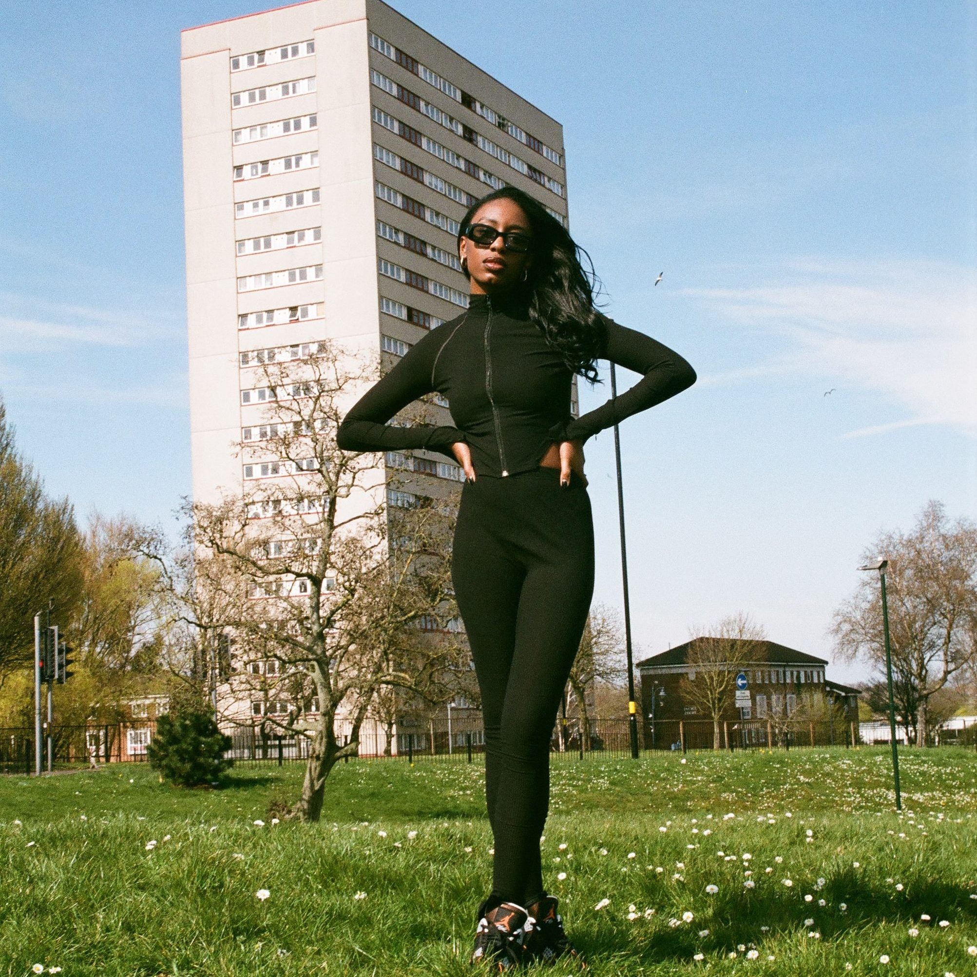 Jaydonclover in all black in front of a tower block.